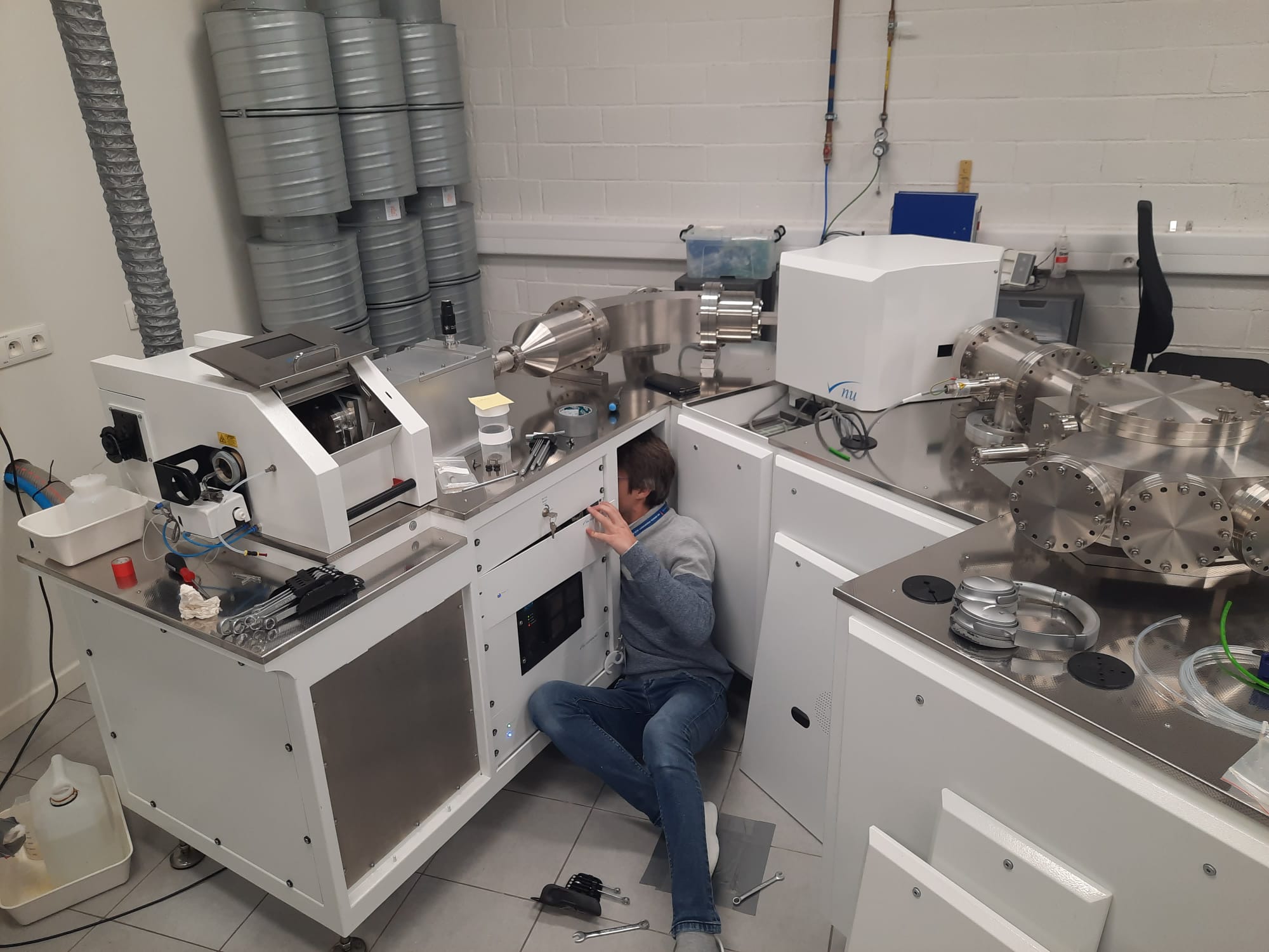 Technician performing maintenance on a high-precision mass spectrometer in a laboratory setting with advanced scientific instruments