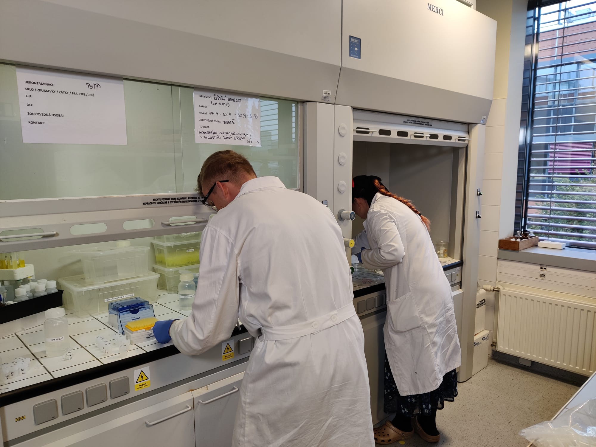 Scientists in protective lab coats working under fume hoods on sample decontamination in a modern laboratory