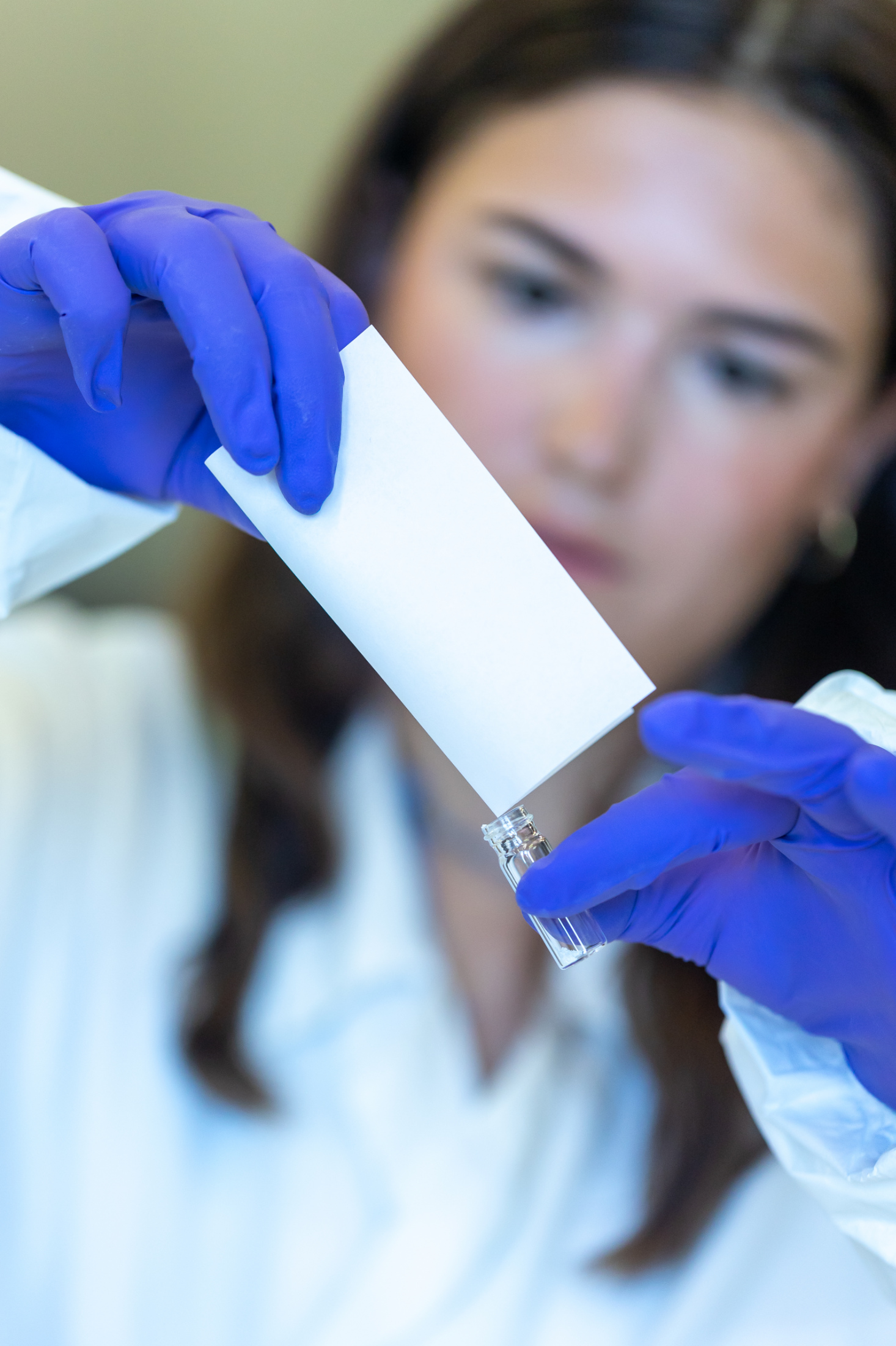 Scientist wearing blue gloves transferring a sample into a small vial using a piece of paper in a laboratory.